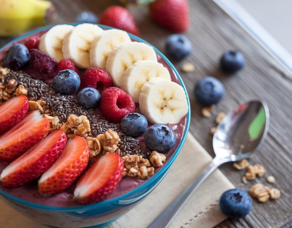 A vibrant vitality bowl with acai, fresh fruits, granola, and honey, placed on a wooden table surrounded by fresh ingredients.