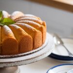 A golden crack cake on a white cake stand, glazed and garnished with powdered sugar and mint leaves.